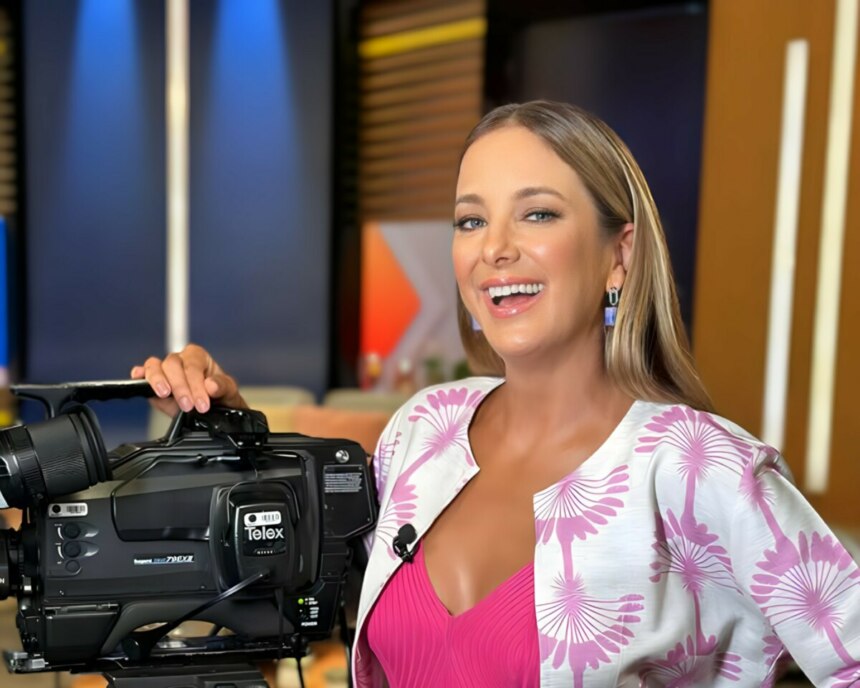 Ticiane Pinheiro sorrindo no cenário do Hoje em Dia ao lado de câmera profissional da RECORD.