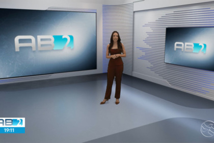 Nathalia Lopes no centro do cenário virtual do AB2, da TV Asa Branca Alagoas, que mostra falhas de recorte na roupa da apresentadora com uma mancha branca