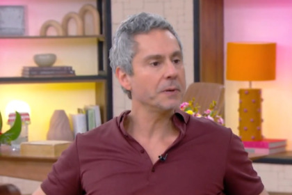O ator Alexandre Nero, de cabelos grisalhos, em entrevista no cenário colorido do programa Mais Você. Ele veste uma camisa polo vinho.