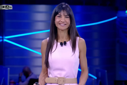 Amanda Klein de vestido rosa no cenário do RedeTV! News. Ela está sorridente