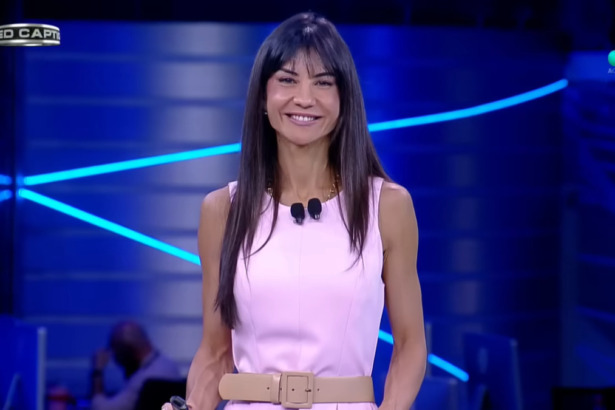 Amanda Klein de vestido rosa no cenário do RedeTV! News. Ela está sorridente