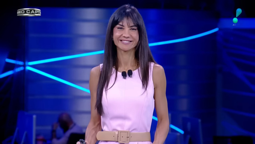 Amanda Klein de vestido rosa no cenário do RedeTV! News. Ela está sorridente