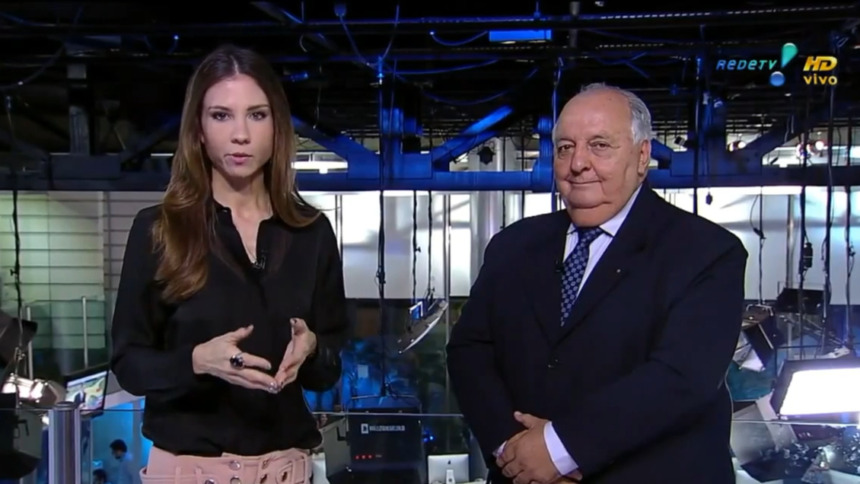 Amanda Klein de blusa preta ao lado de um comentarista de terno no estúdio do RedeTV! News no dia em que virou meme