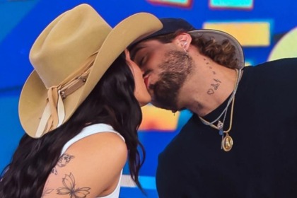 Os cantores Ana Castela (de chapéu de cowboy) e Zé Felipe (de boné) se beijam intensamente no palco do programa Domingo Legal.