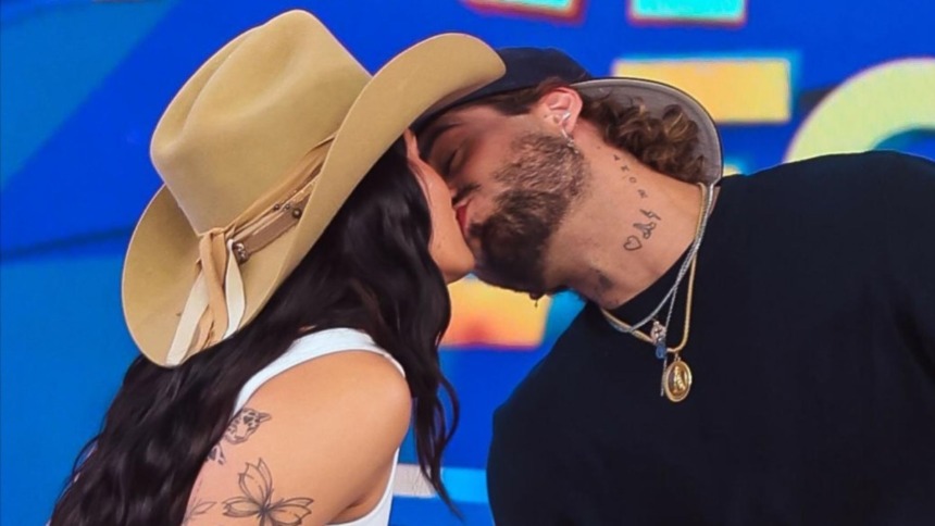 Os cantores Ana Castela (de chapéu de cowboy) e Zé Felipe (de boné) se beijam intensamente no palco do programa Domingo Legal.