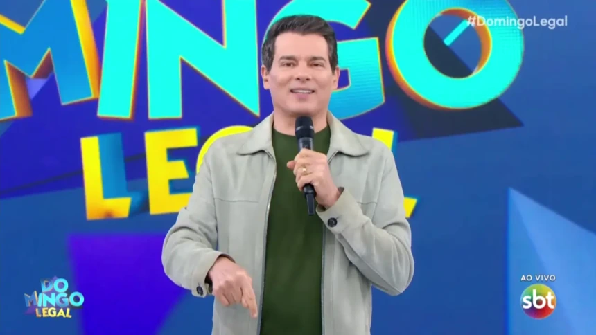 Celso Portiolli apresentando o Domingo Legal e sorrindo apontando para baixo
