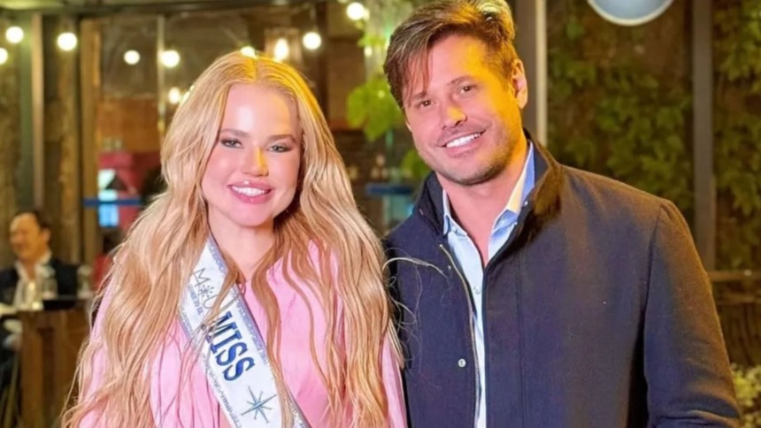 O ator Dado Dolabella (blazer azul-marinho e camisa social azul-clara) posa ao lado da modelo e Miss Marcela Tomaszewski (cabelos loiros longos, blusa rosa e faixa de Miss). Ambos estão sorridentes, em um ambiente externo noturno com luzes de fundo.
