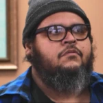 Dominic Hernandez no reality Quilos Mortais da Record, usando gorro cinza e camisa xadrez