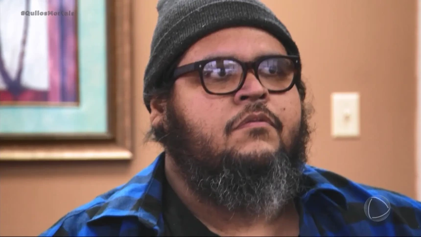 Dominic Hernandez no reality Quilos Mortais da Record, usando gorro cinza e camisa xadrez