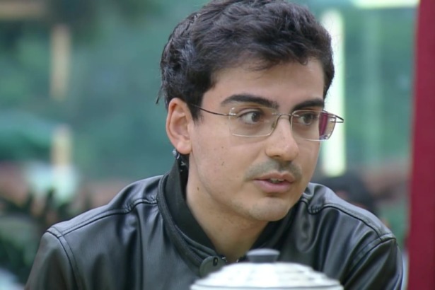 Dudu Camargo, de óculos e jaqueta preta, na cozinha de A Fazenda