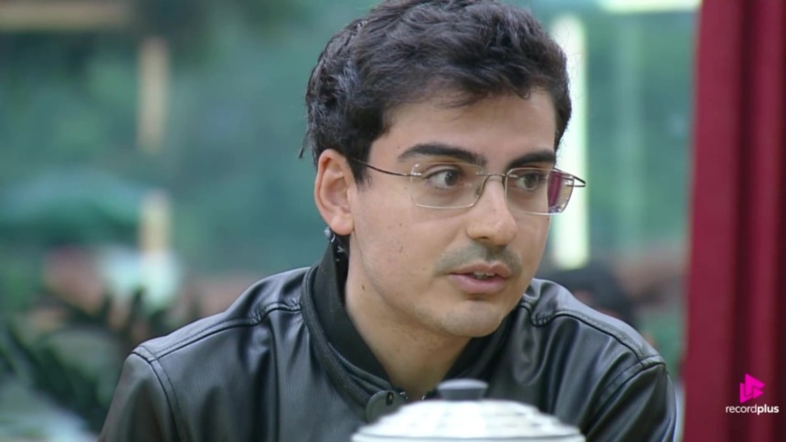 Dudu Camargo, de óculos e jaqueta preta, na cozinha de A Fazenda