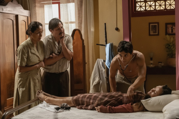 Túlio examina Estela que está deitada desmaiada em uma cama de uma casa simples em cena de Êta Mundo Melhor
