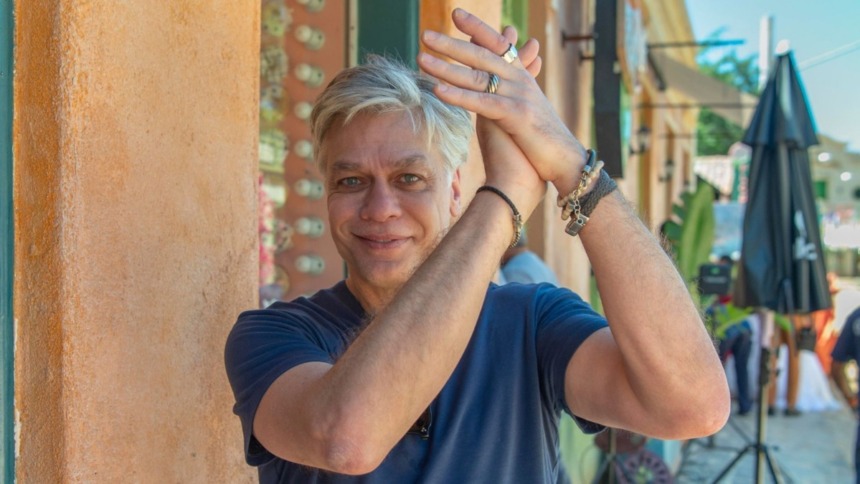 Ator Fabio Assunção, sorridente e gesticulando com as mãos no alto