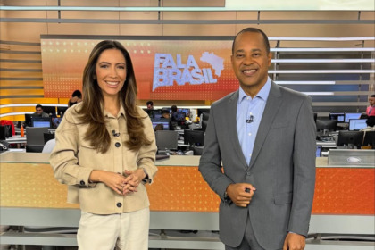 Paloma Poeta e Luiz Fara Monteiro sorridentes em pé no cenário do Fala Brasil