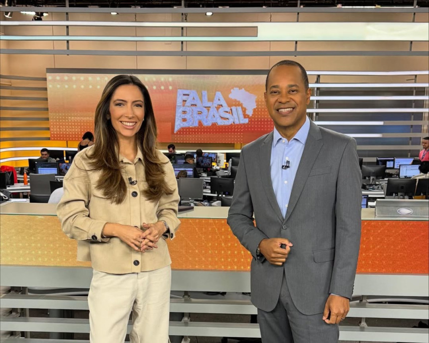 Paloma Poeta e Luiz Fara Monteiro sorridentes em pé no cenário do Fala Brasil