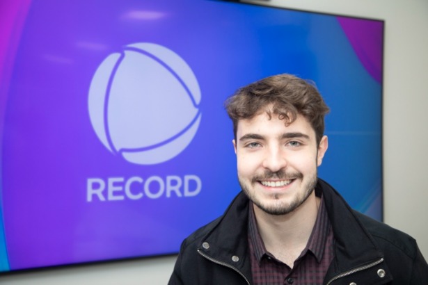 João Augusto Liberato em frente a uma TV com o logo da RECORD