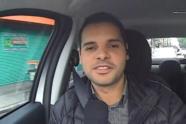 O repórter João Netto em entrada ao vivo no Bom Dia SP. Ele está dentro de um carro, de jaqueta, falando no microfone.