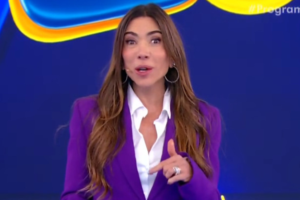 A apresentadora Patricia Abravanel no palco, de blazer roxo sobre camisa branca, sorri e aponta. O fundo é azul, da Tele Sena de Primavera.