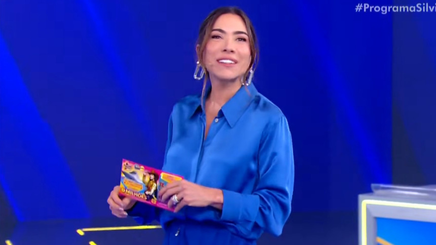 A apresentadora Patricia Abravanel usa uma blusa azul e segura uma Tele Sena na mão, em trecho do terceiro sorteio