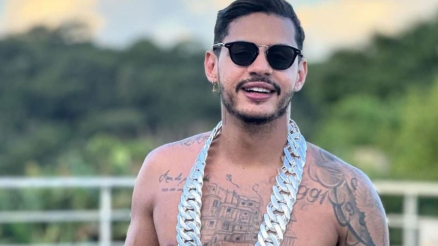 Rapper Hungria sem camisa, de óculos escuros e um colar prateado grosso. Ele tem barba e exibe tatuagens no peito.