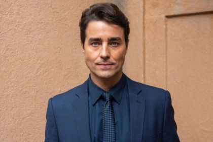 O ator Ricardo Pereira em um retrato. Ele veste um terno azul-marinho e gravata, olhando para a câmera com um olhar sério e intenso.