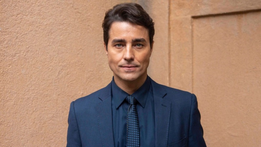 O ator Ricardo Pereira em um retrato. Ele veste um terno azul-marinho e gravata, olhando para a câmera com um olhar sério e intenso.