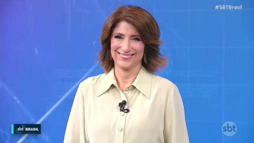 Simone Queiroz sorrindo no centro do cenário do SBT Brasil
