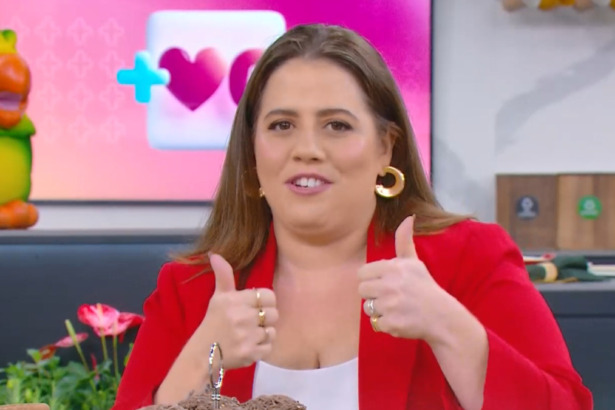 Tati Machado sorri e faz "joinha" com as duas mãos. Ela veste um blazer vermelho no cenário colorido do programa Mais Você, anunciando que vai divulgar Três Graças no intervalo de Vale Tudo