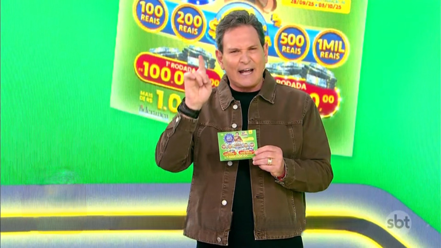 Luis Ricardo no estúdio temático na cor verde apresentando a edição 72 da Tele Sena Semanal. Ele segura o bilhete da edição