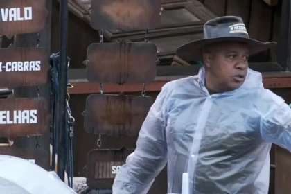 Toninho com capa de chuva e chapéu de fazendeiro apontando para os peões durante delegação em A Fazenda 17