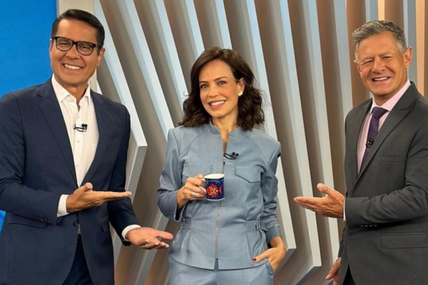 Os apresentadores Willian Leite (terno azul-marinho e óculos), Fabiana Oliveira (terninho cinza-azulado, segurando uma caneca) e Diógenes Lucca (terno cinza, gravata roxa) sorriem e posam no estúdio do Balanço Geral Manhã.