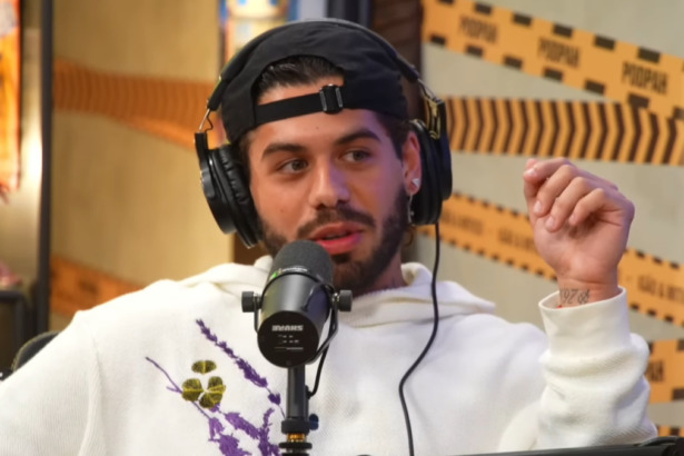 O cantor Zé Felipe em entrevista no PodPah. Ele usa boné, fones de ouvido e um moletom branco com estampa, falando ao microfone.