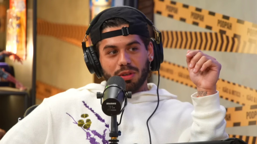O cantor Zé Felipe em entrevista no PodPah. Ele usa boné, fones de ouvido e um moletom branco com estampa, falando ao microfone.