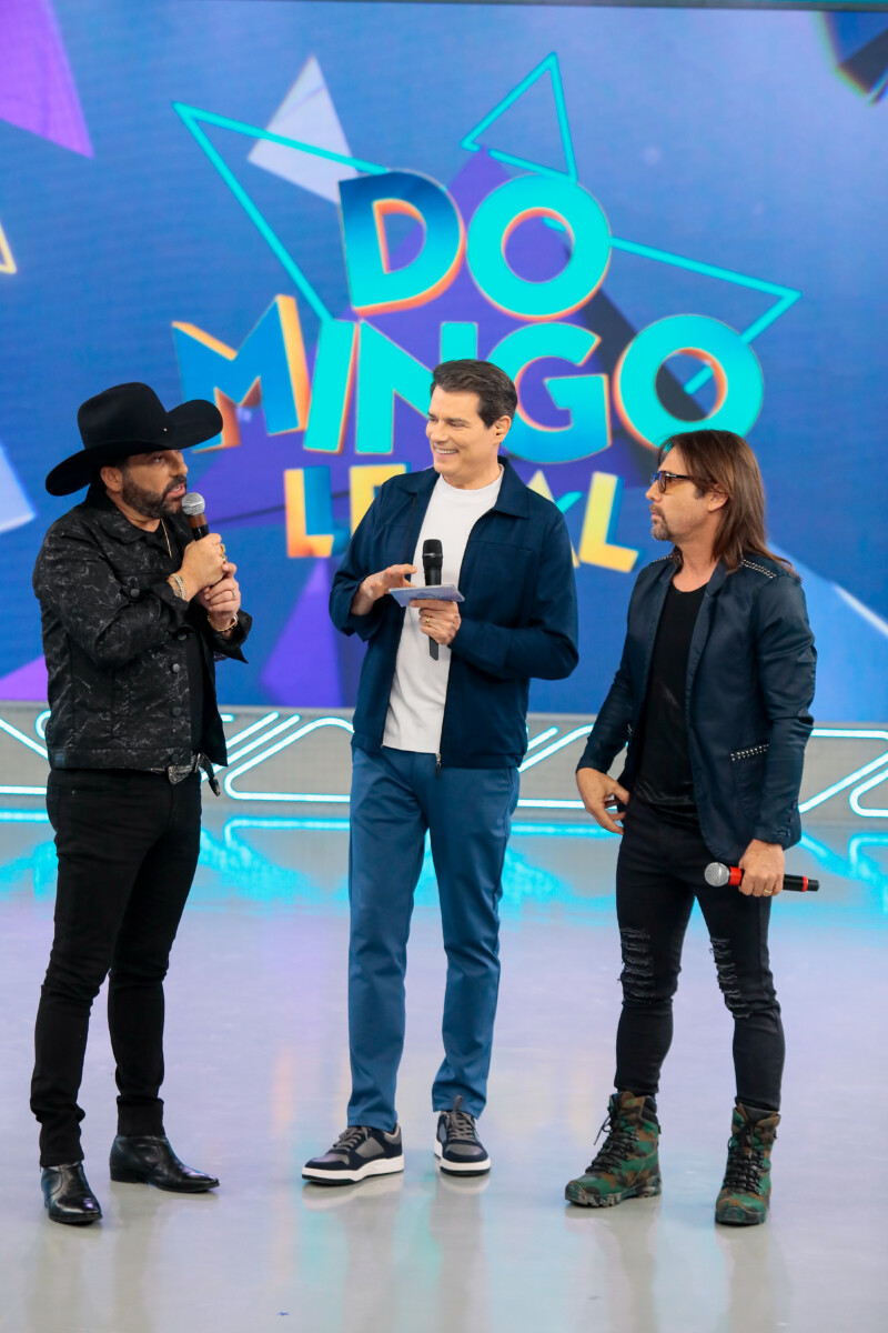 Celso Portiolli em pé no palco do Domingo Legal conversando com Edson & Hudson