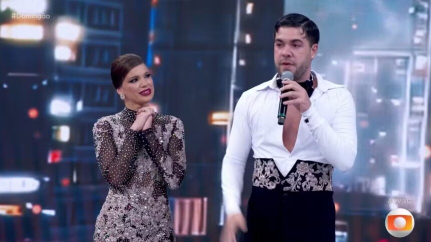 O influenciador Alvaro e a bailarina Mariana Torres no palco do Dança dos Famosos, com Alvaro falando ao microfone e visivelmente emocionado após apresentação