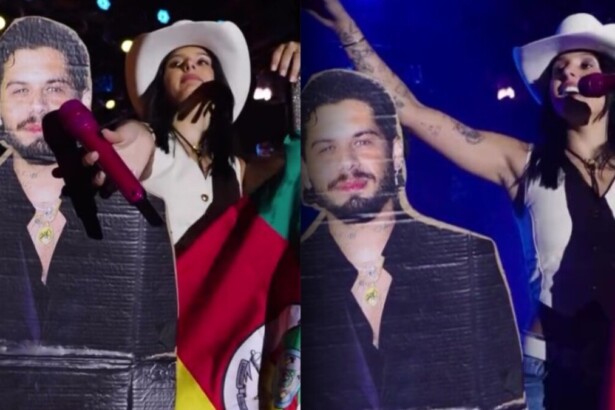 Cantora Ana Castela no palco com chapéu de cowboy e bandeira, ao lado de um boneco de papelão do cantor Zé Felipe, em show