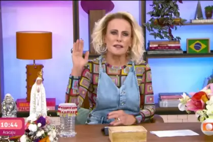 Ana Maria Braga levanta a mão esquerda enquanto apresenta o Mais Você sentada na bancada