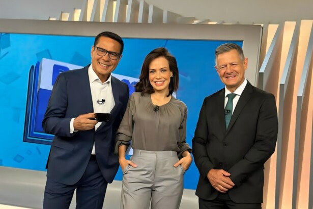 Willian Leite, Fabiana Oliveira e Comandante Lucca em pé em frente ao telão do Balanço Geral Manhã, ambos sorriem