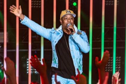 Cantor Márcio Victor da banda Psirico, cantando no palco com jaqueta jeans e boné, gesticulando para o público com as mãos levantadas