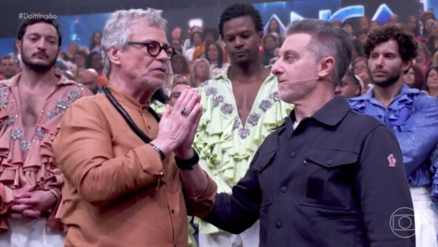 Carlinhos de Jesus e Luciano Huck em pé, em frente a plateia, durante a Dança dos Famosos no Domingão