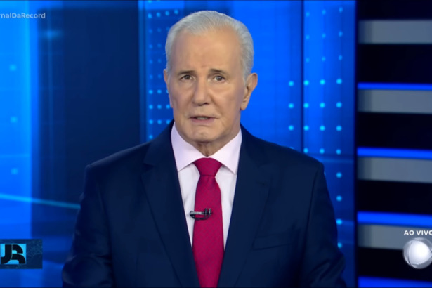 Celso Freitas, com semblante sério, de gravata vermelha no centro do cenário do Jornal da Record. Ele é o novo ancora do SBT News