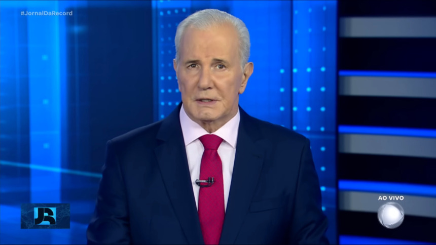Celso Freitas, com semblante sério, de gravata vermelha no centro do cenário do Jornal da Record. Ele é o novo ancora do SBT News