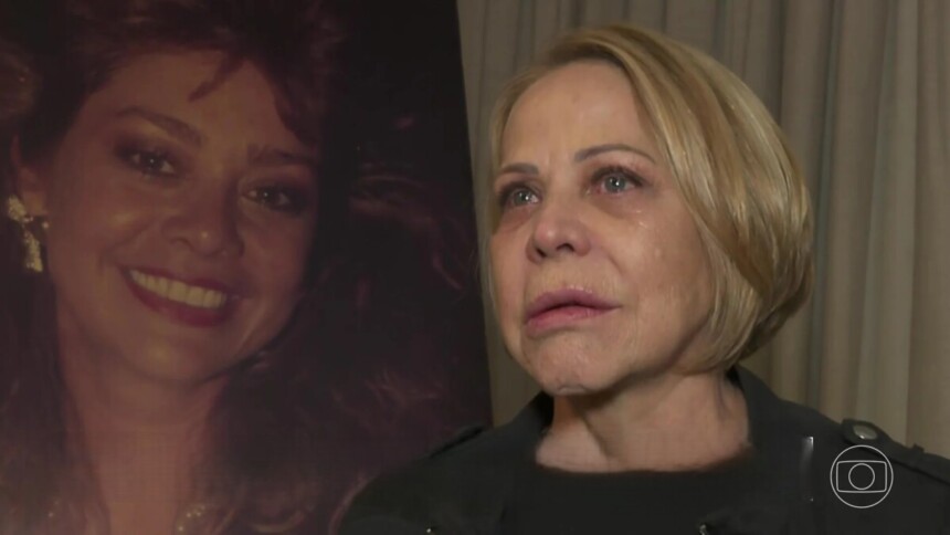 Claudete Troiano com lágrimas nos olhos em frente a um quadro com foto de Ione Borges no velório da apresentadora