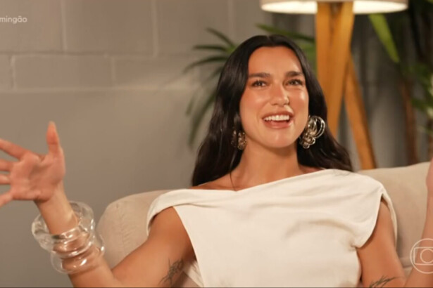 Cantora internacional Dua Lipa sorrindo e gesticulando durante entrevista para o programa Domingão com Huck