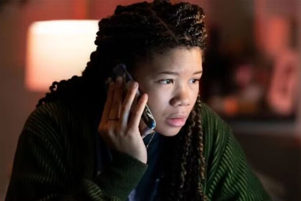 Atriz Storm Reid como June Allen, a protagonista do filme de suspense Desaparecida, falando ao telefone com expressão de preocupação em ambiente escuro