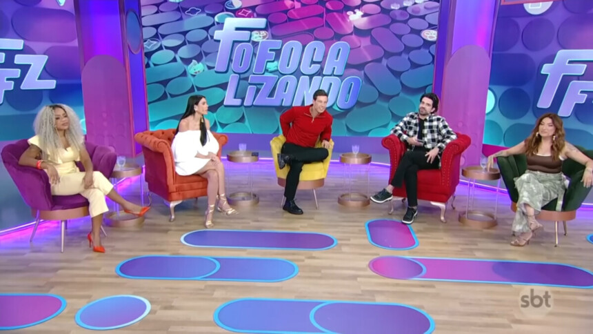 Apresentadores do Fofocalizando no SBT sentados em suas poltronas num cenário com cores predominantemente em tons de lilás e azul