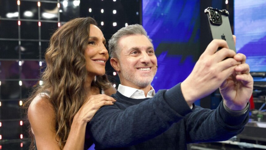 Cantora Ivete Sangalo e apresentador Luciano Huck tirando selfie no palco do programa Domingão com Huck, sorrindo para o celular