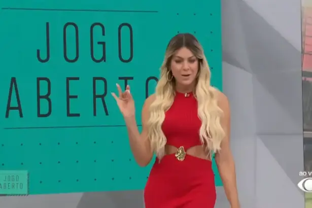 Renata Fana de vestido vermelho em pé na frente do telão do Jogo Aberto