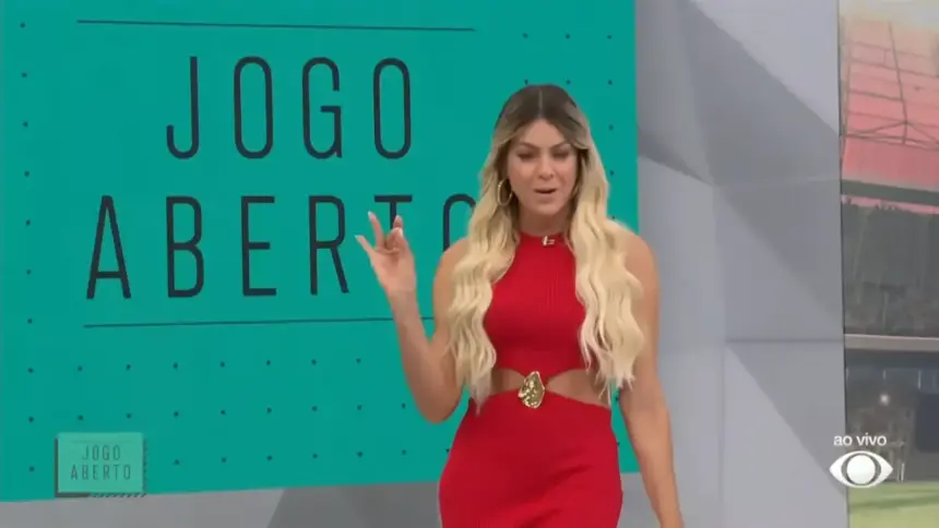 Renata Fana de vestido vermelho em pé na frente do telão do Jogo Aberto