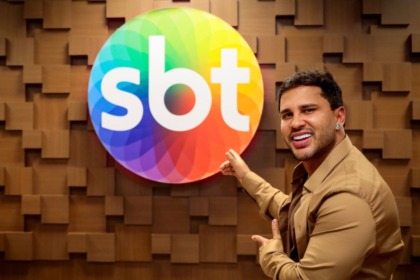 Lucas Guimarães apresentador do Eita, Lucas!, apontando e sorrindo ao lado do logo do SBT em comemoração à renovação de contrato